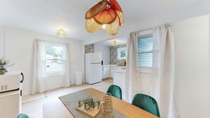 A modern kitchen with white appliances, a dining area with a wooden table and green chairs, and a ceiling light fixture. - The Playmakers Funhouse: HOF Village (Canton)