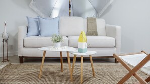 A living room with a light-colored sofa, two small round tables, a decorative umbrella, and a wooden chair. - The Playmakers Funhouse: HOF Village (Canton)