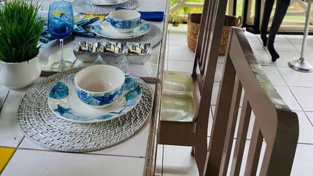 A table set for dining with blue and white tableware, a hanging wicker light fixture, and a view of the sea and trees in the background. - 1 bedroom Beach House at Bluefields Bay (bluefields)