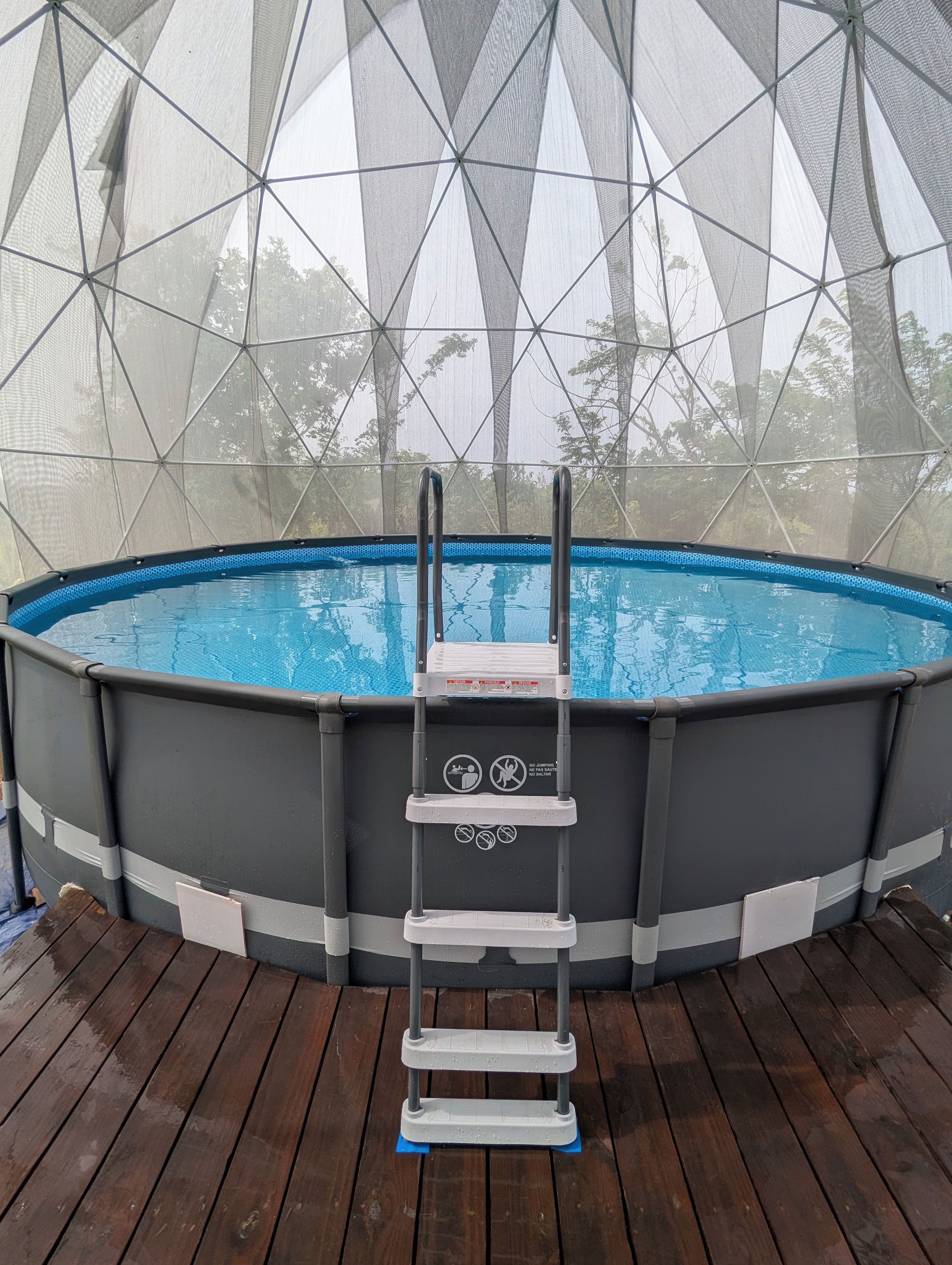 Une piscine hors sol, dotée d’un escalier et entourée d’un filet de protection, installée sur une terrasse en bois.