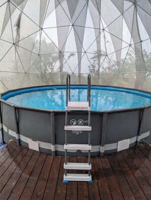 Une piscine hors sol, dotée d’un escalier et entourée d’un filet de protection, installée sur une terrasse en bois.