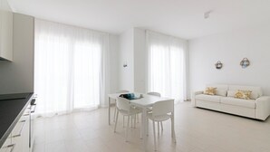 A modern, minimalist living space with a dining area, a sofa, and a kitchen counter. - Rivazzurra Homes - 24 (Litorale Nord)