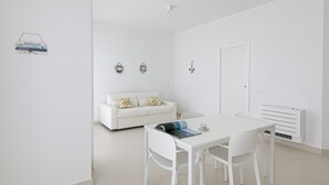 A minimalist room with a white sofa, a dining table with chairs, and a radiator. - Rivazzurra Homes - 24 (Litorale Nord)