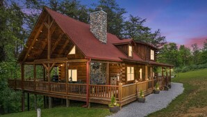 A log cabin with a stone chimney, wooden deck, and outdoor seating area.