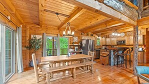 A spacious wooden cabin with a large dining table, kitchen area, and a cozy seating area.