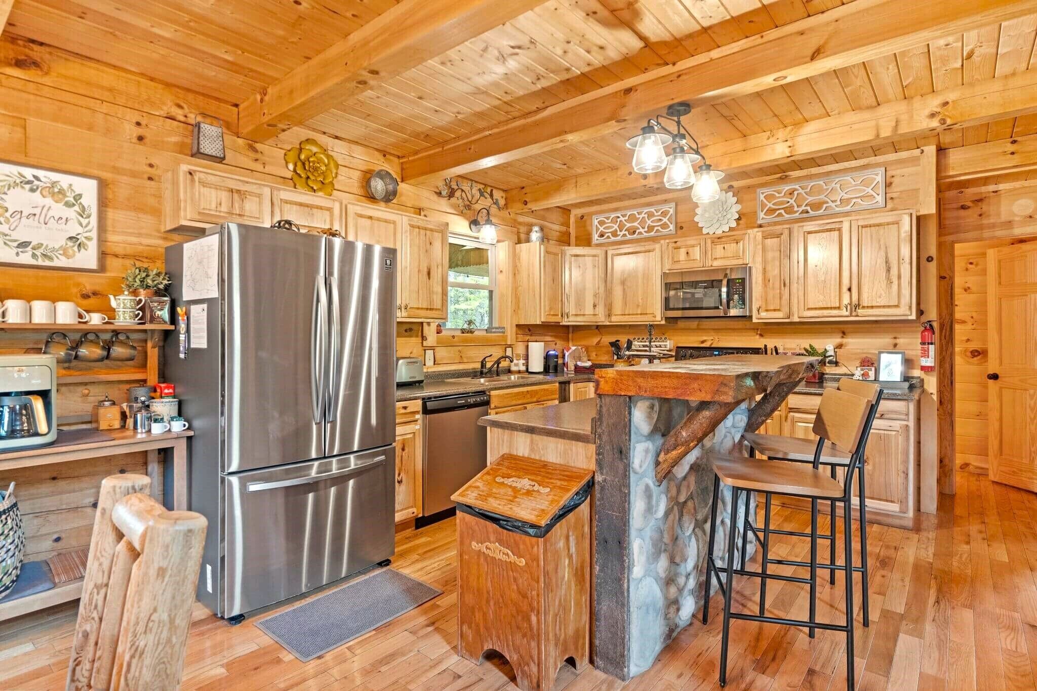 A wooden cabin kitchen with a large refrigerator, wooden cabinets, a stone island, and bar stools.