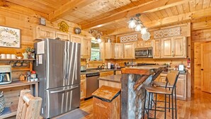 A wooden cabin kitchen with a large refrigerator, wooden cabinets, a stone island, and bar stools.