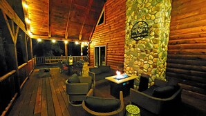 A log cabin with a stone wall, outdoor seating, and a fire feature.