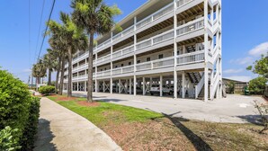 A multi-story building with a white exterior, multiple balconies, and a covered parking area. - Walk to Beach & Pier: Quiet Retreat in Surf City (Surf City)