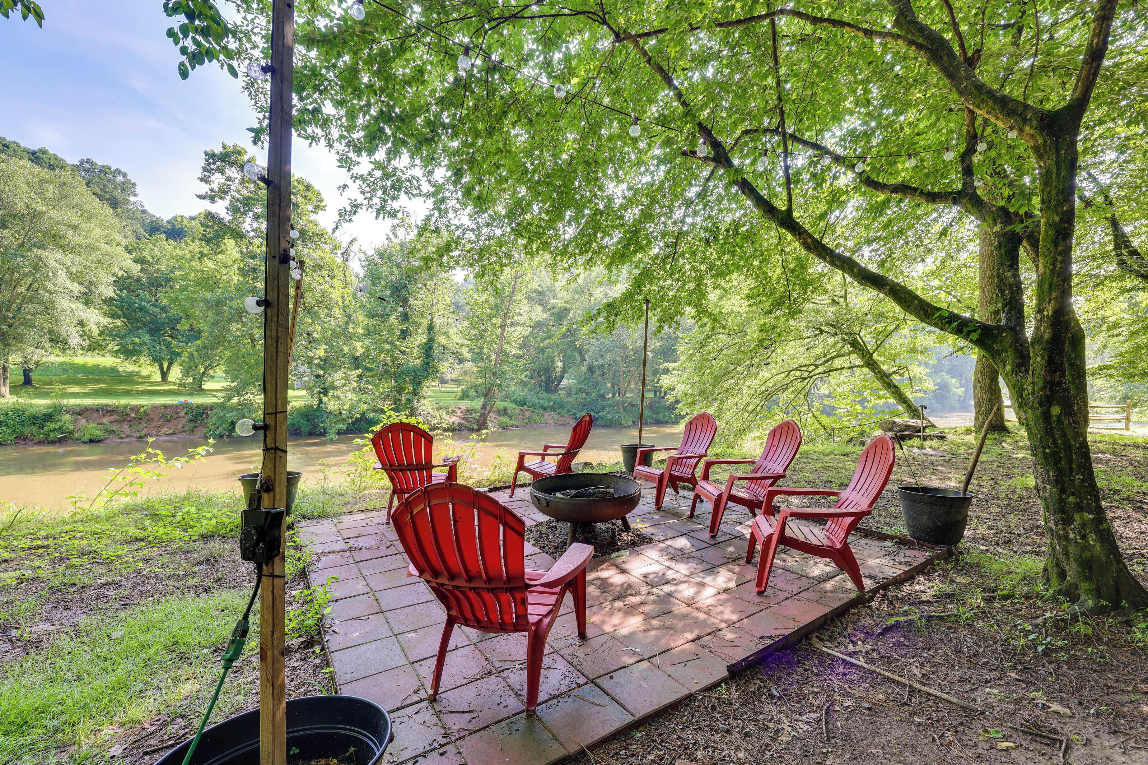 An outdoor patio with red Adirondack chairs, a fire pit, and a view of a river.