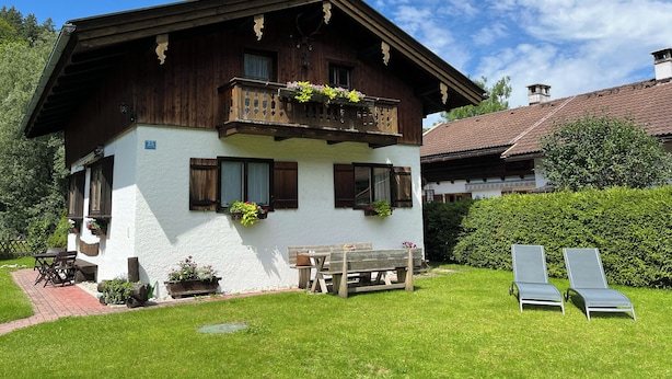 A two-story chalet with a balcony, wooden shutters, and a garden with a bench and lounge chairs. - Vacation home Anni - a retreat to relax and enjoy nature at Lake Tegernsee (Kreuth)