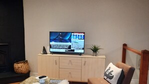 En stue med et fjernsyn på et træskab, en læderstol i brunt, en blød, hvid pude og et lille bord med en fjernbetjening.