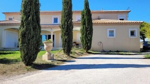 Un edificio a due piani con tetto in tegole, vialetto e alte cipressi.