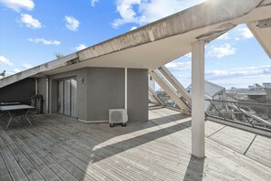 A rooftop terrace with a grill, a table, and an air conditioning unit.