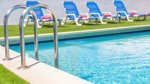 A swimming pool with a tiled edge, a metal ladder, and several lounge chairs with towels. - Modern villa with a welcoming atmosphere (Albufeira)