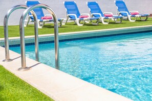 A swimming pool with a tiled edge, a metal ladder, and several lounge chairs with towels. - Modern villa with a welcoming atmosphere (Albufeira)