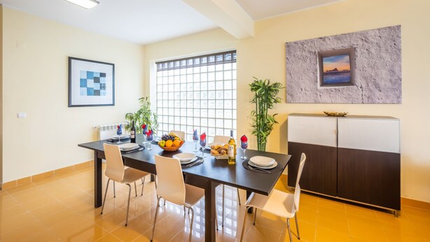 A dining area with a table set for four, chairs, a buffet table with fruits and a bottle of wine, and a refrigerator. - Modern villa with a welcoming atmosphere (Albufeira)