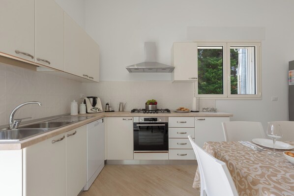 Une cuisine moderne avec des meubles blancs, un évier en acier inoxydable, un four et une fenêtre donnant sur les arbres.