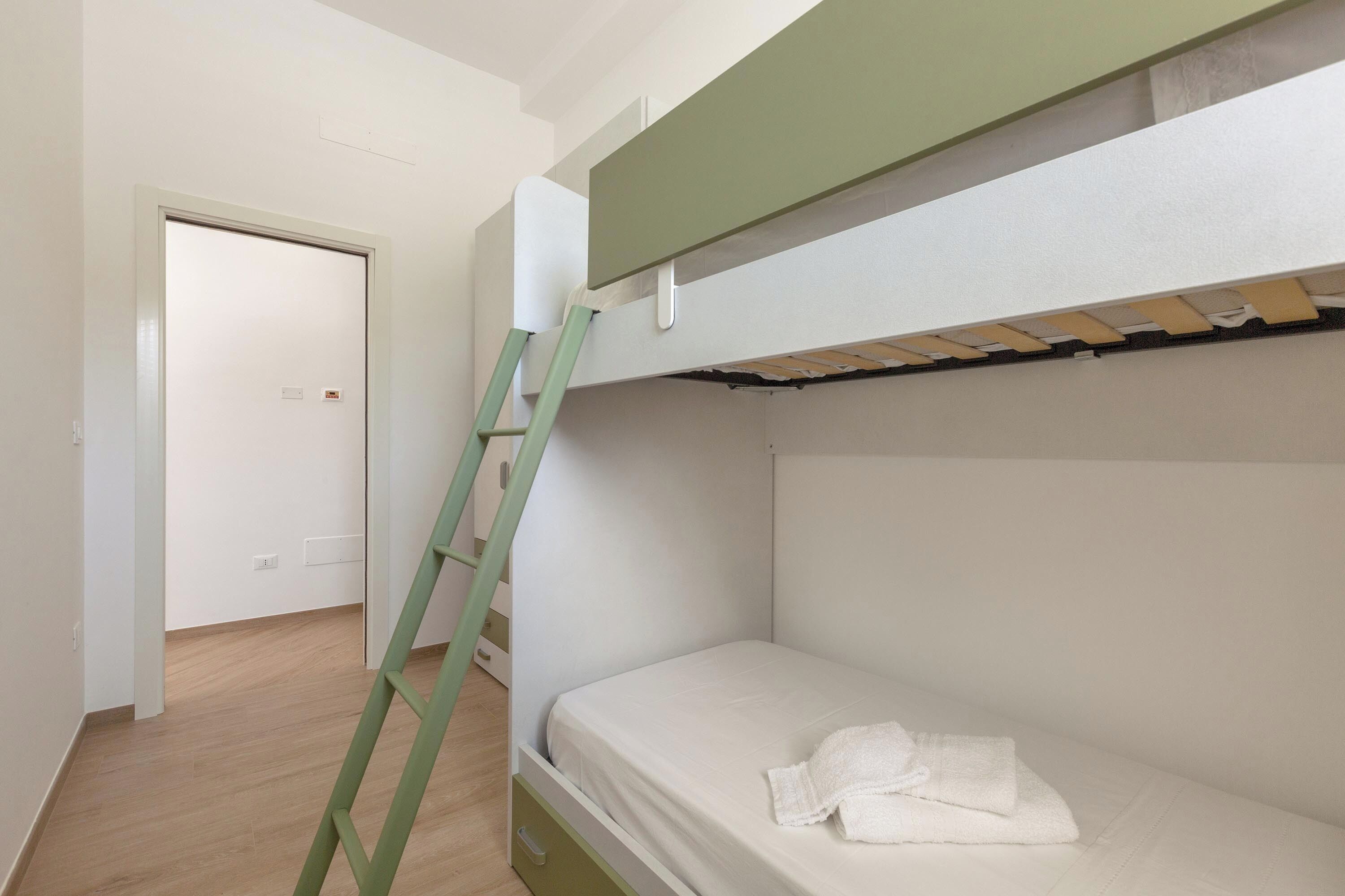 Uma cama beliche com escada, colchão e toalha brancos.