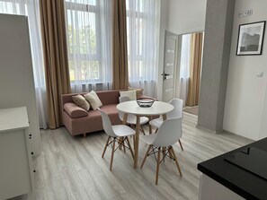 A modern living room with a sofa, chairs, a round table, and a window with sheer curtains.