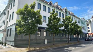 Un immeuble à plusieurs étages, doté d’une façade blanche et de bordures vertes, de grandes fenêtres et d’un toit plat.