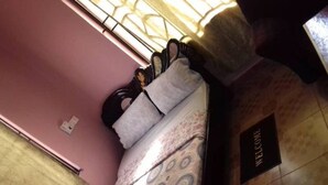 Una habitación con pared rosa, una cama con colcha estampada, un felpudo y una ventana con barrotes.