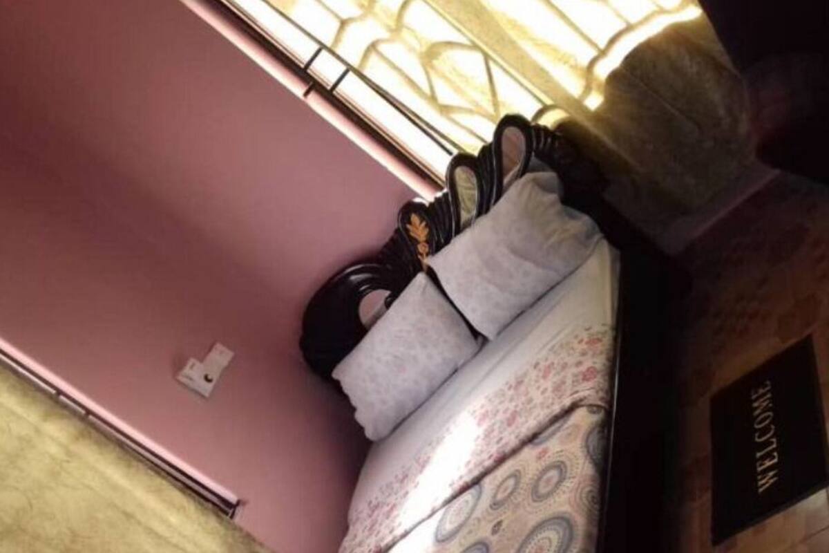 Una habitación con pared rosa, una cama con colcha estampada, un felpudo y una ventana con barrotes.