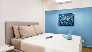 Un dormitorio con cama, mesita de noche, aire acondicionado instalado en la pared y un cuadro.