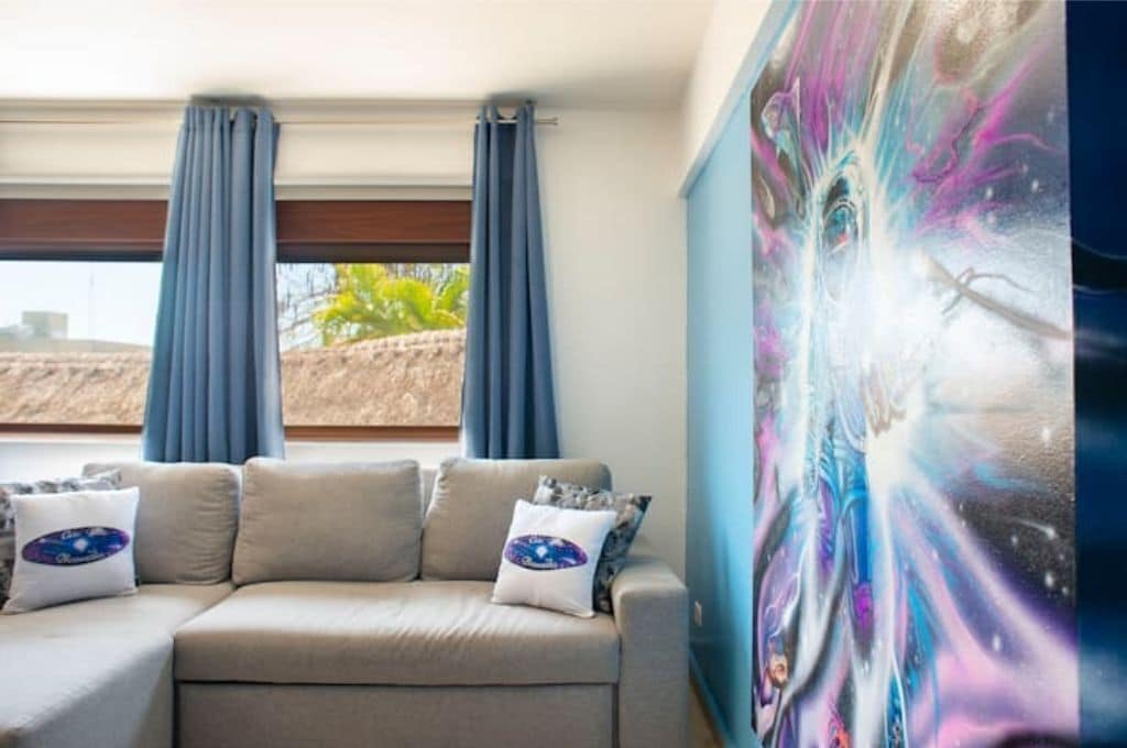 A room with a beige sofa, two blue curtains, and a large abstract painting on the wall.