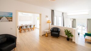 Un salon moderne comprenant un coin repas, un canapé en cuir noir, une plante en pot et un plancher en bois.