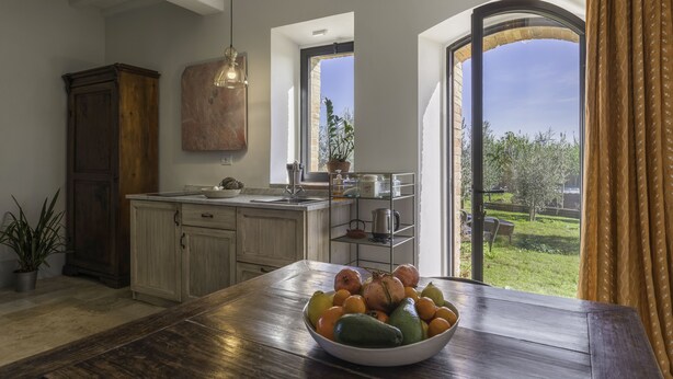 A kitchen with a wooden table, a bowl of fruit, and a view of the outdoors. - Lina - Podere Ribatti Casole D'elsa (Casole d'Elsa)