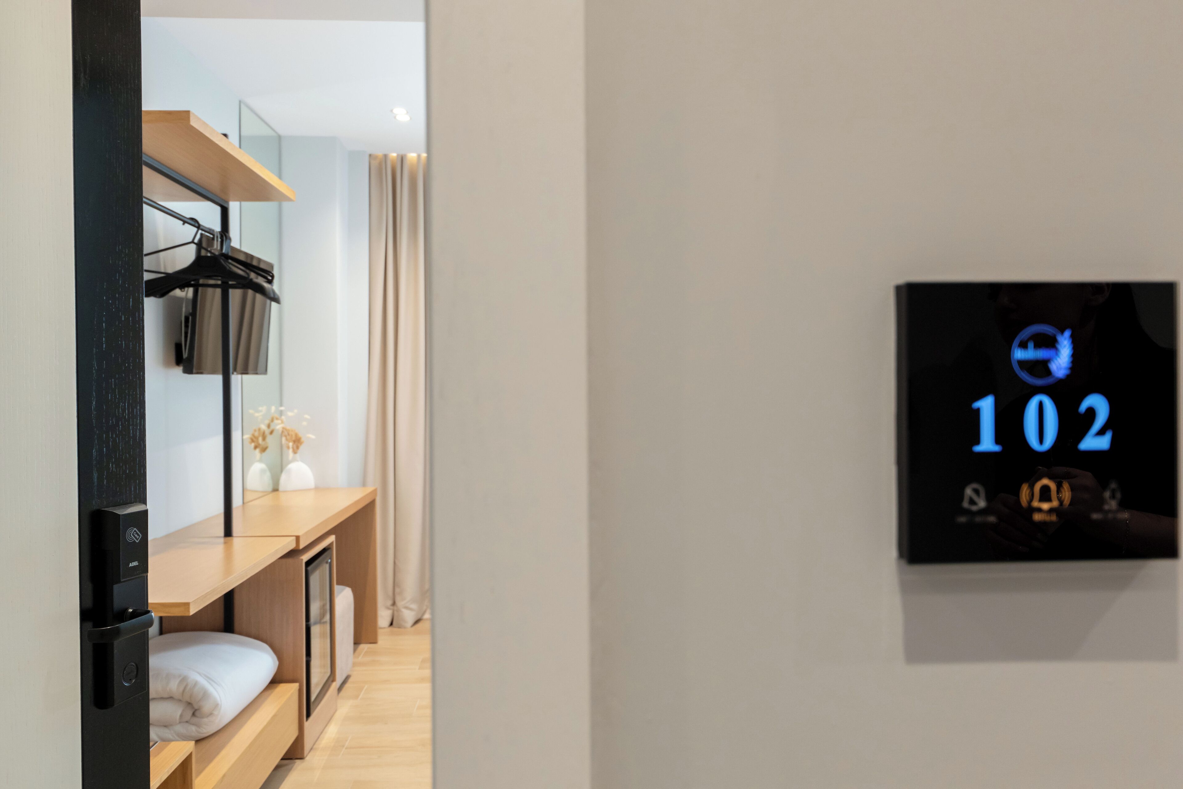 A hotel room with a bed, a desk, a mirror, and a digital display showing room number 102.
