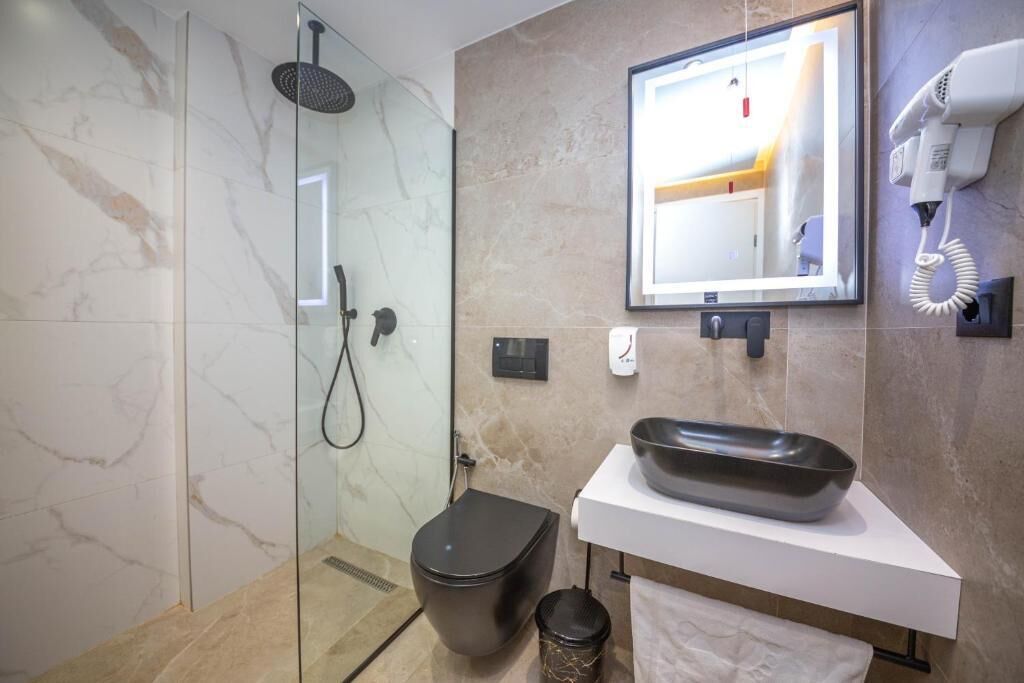 Une salle de bain moderne avec une douche à parois de verre, des toilettes, un lavabo avec un receveur, un miroir et un sèche-cheveux fixé au mur.
