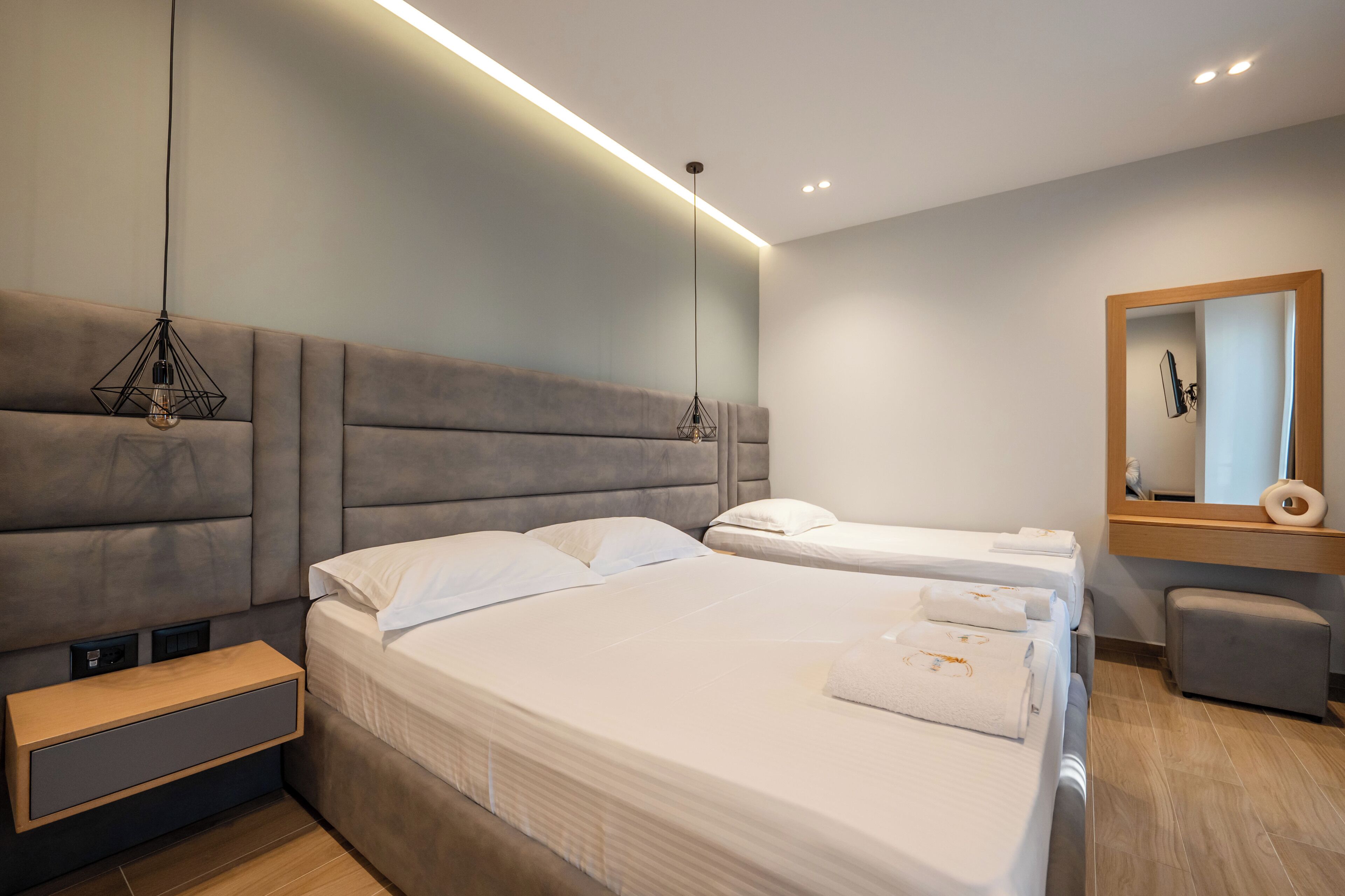 A modern hotel room with a large bed, bedside tables, a mirror, and a bench.