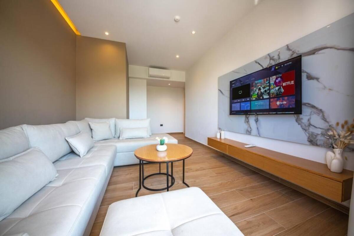 A modern living room with a sectional sofa, a round coffee table, and a mounted TV displaying streaming services.