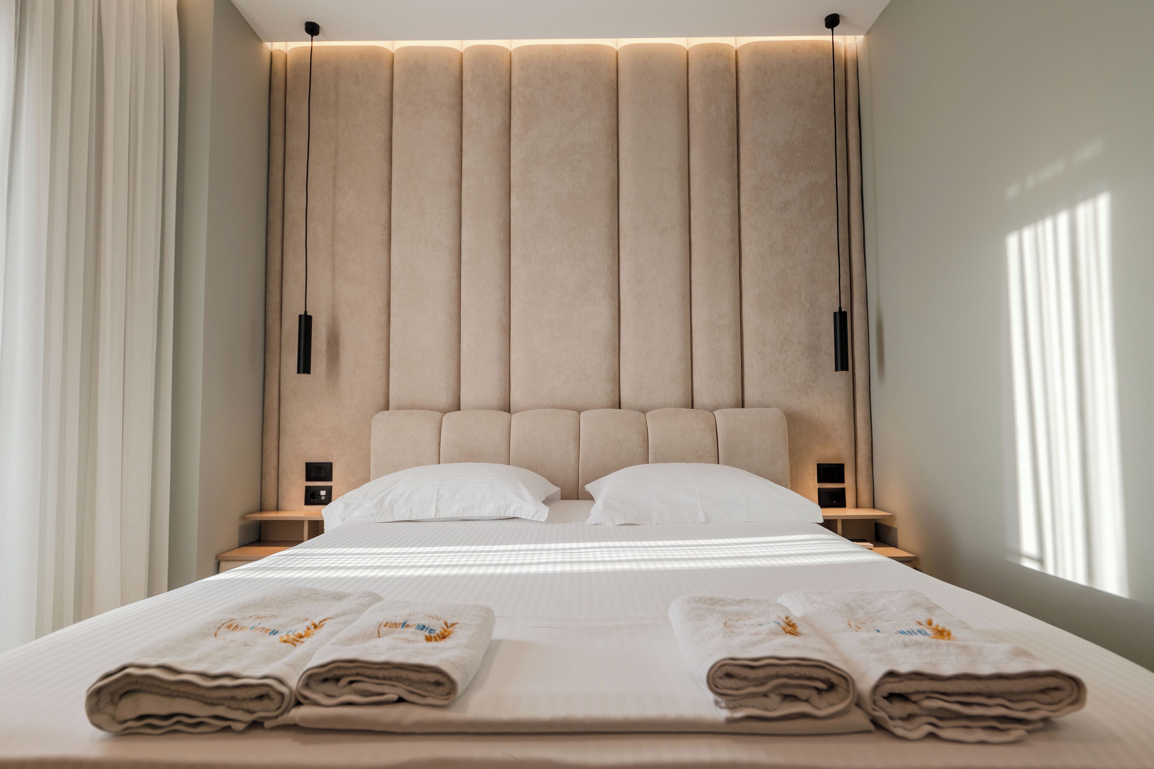 A modern hotel room with a large bed, two bedside tables, and a headboard with vertical panels.