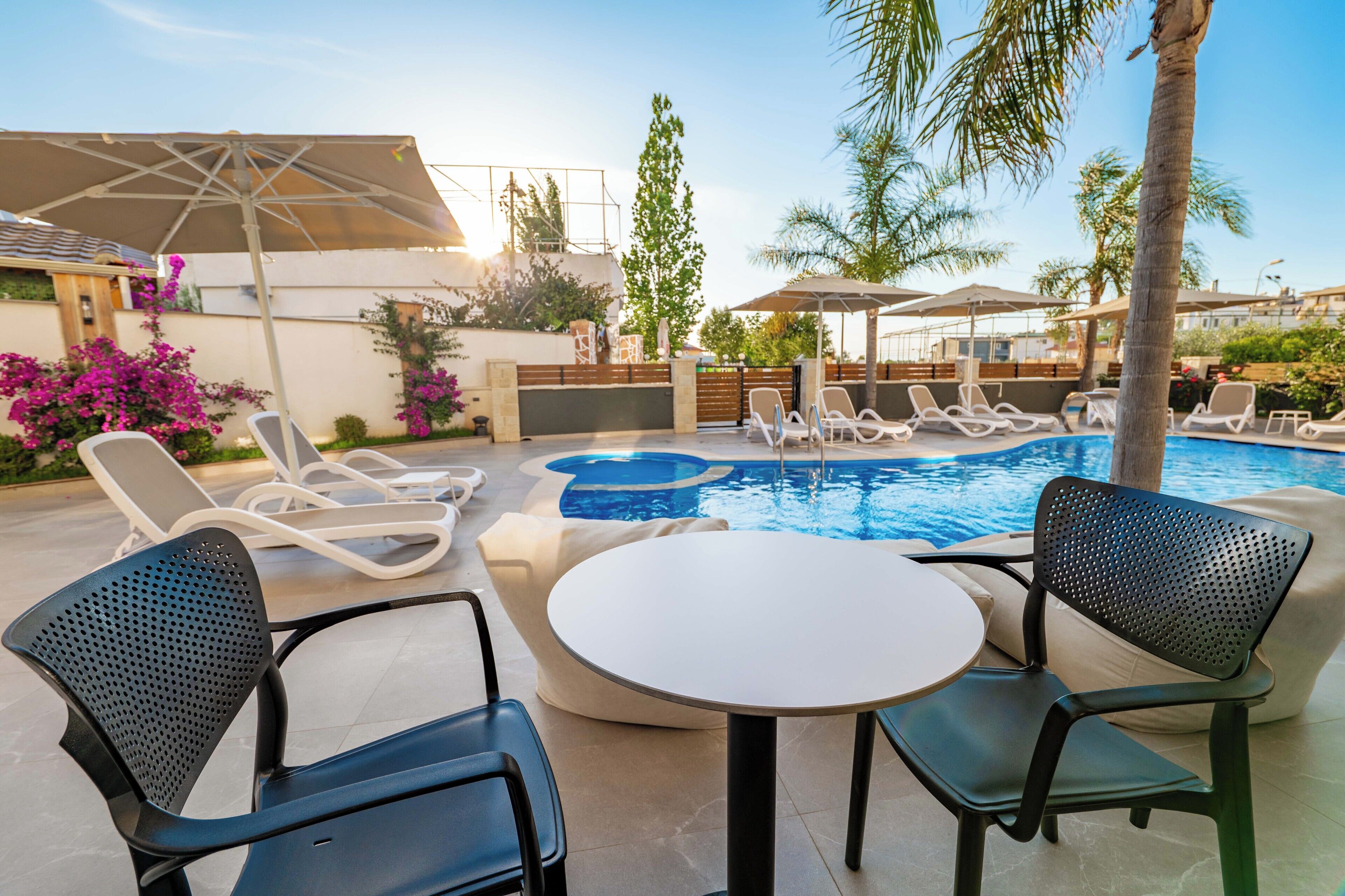 A poolside area with lounge chairs, a table, and umbrellas.