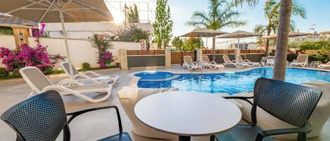 A poolside area with lounge chairs, a table, and umbrellas.