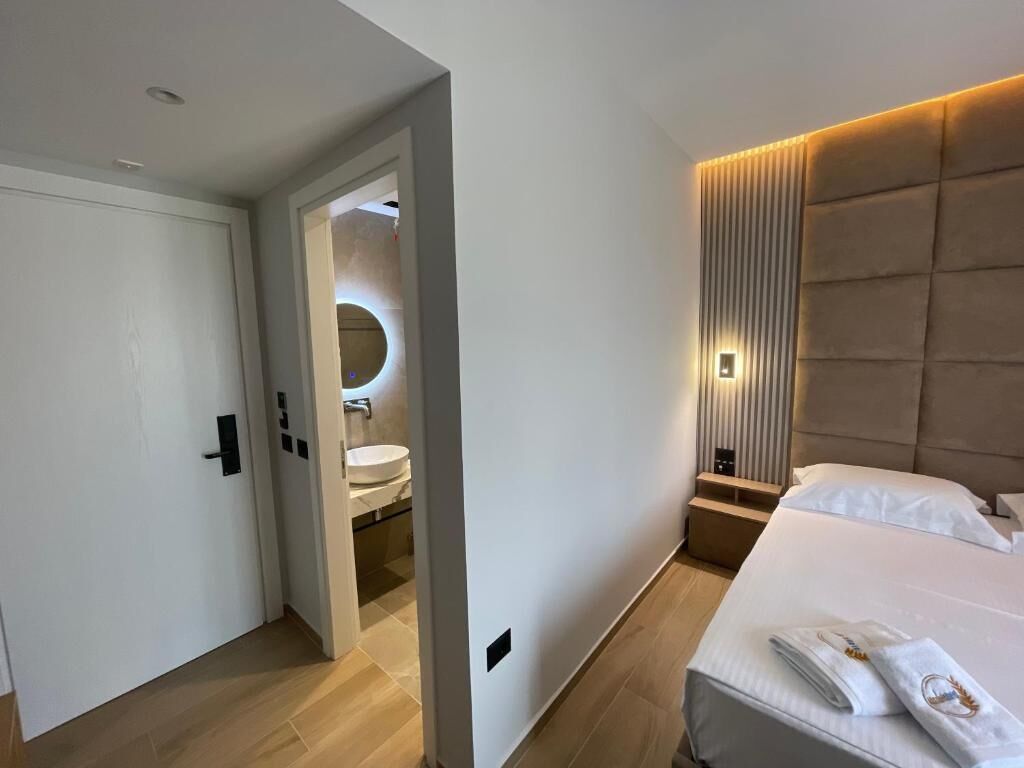 A modern hotel room with a large bed, a bedside table, a nightstand, and a wall-mounted light fixture.