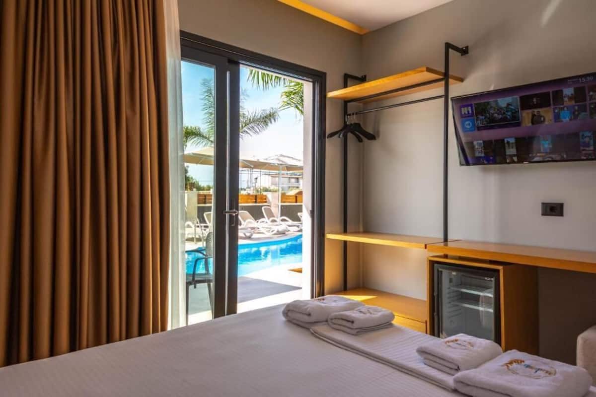 A hotel room with a bed, a TV, a mini-fridge, and a view of an outdoor pool area.