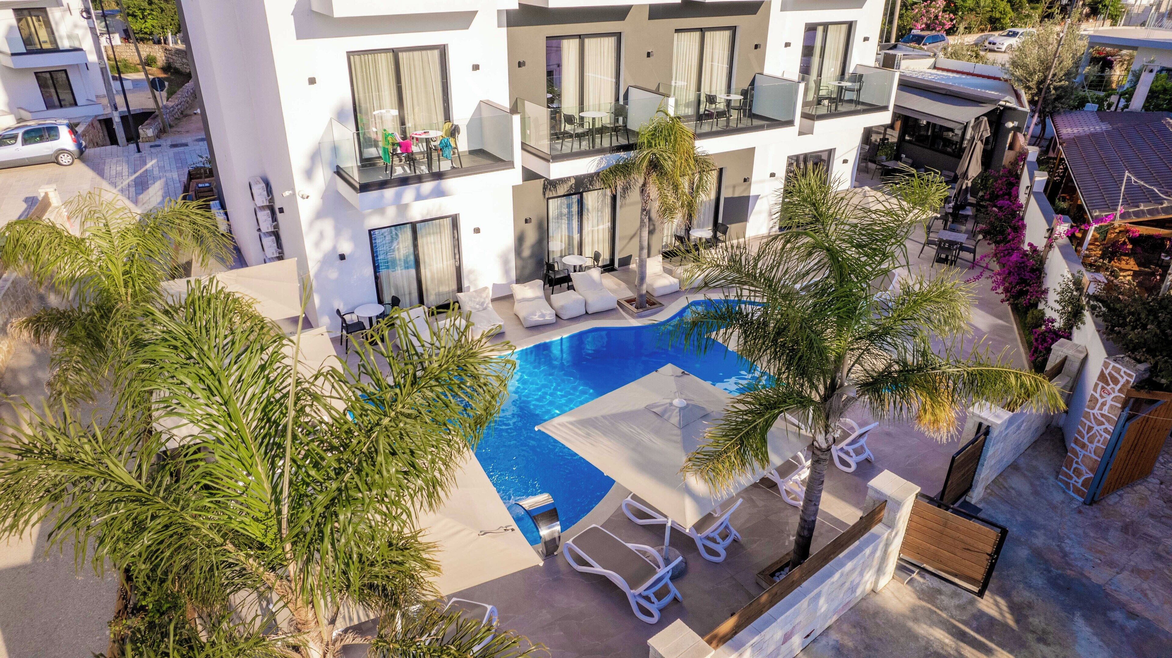 A modern hotel with a swimming pool surrounded by palm trees and lounge chairs.