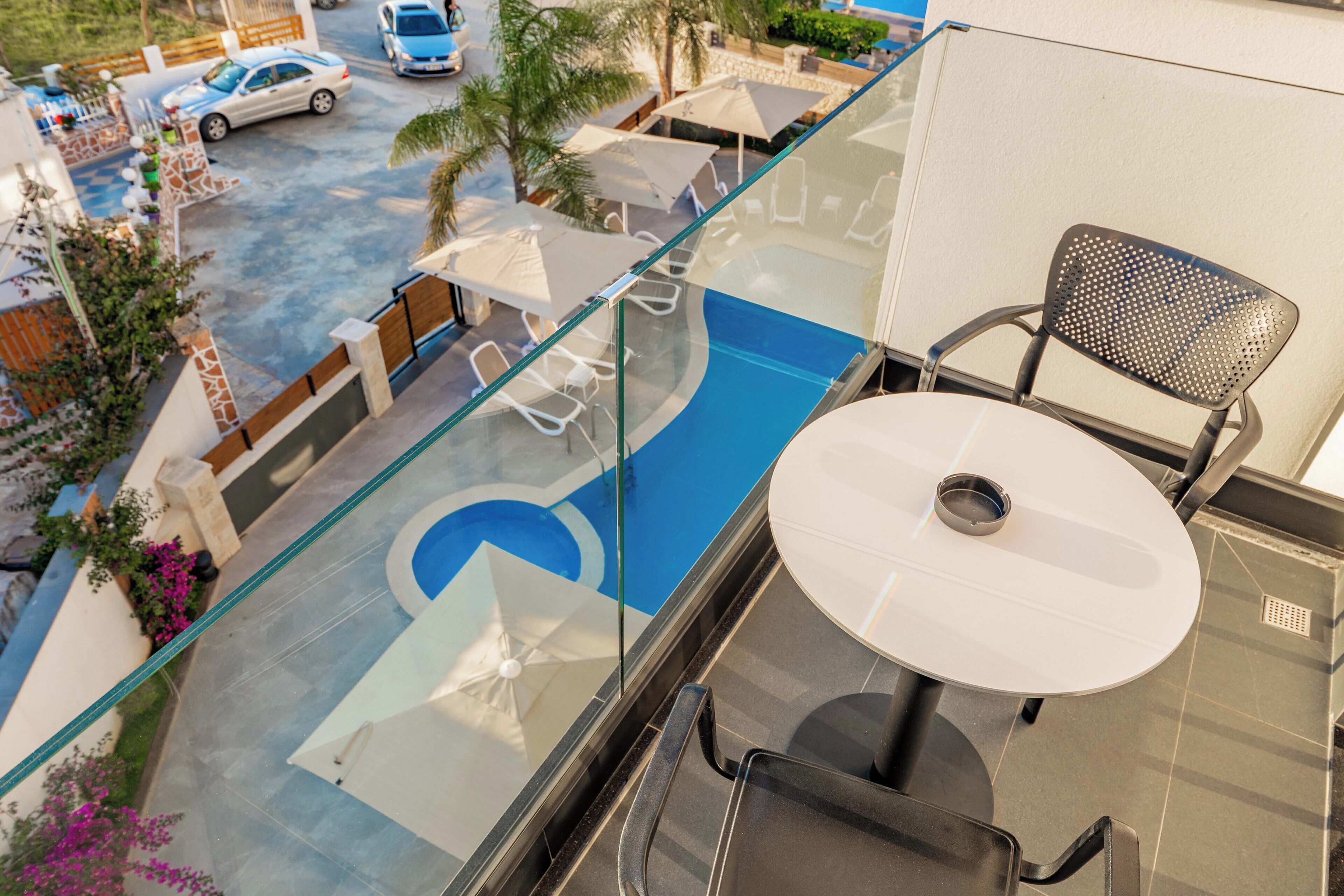 Un balcon doté d’une rambarde en verre donnant sur une piscine, avec une table et des chaises.