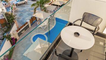 Un balcon doté d’une rambarde en verre donnant sur une piscine, avec une table et des chaises.