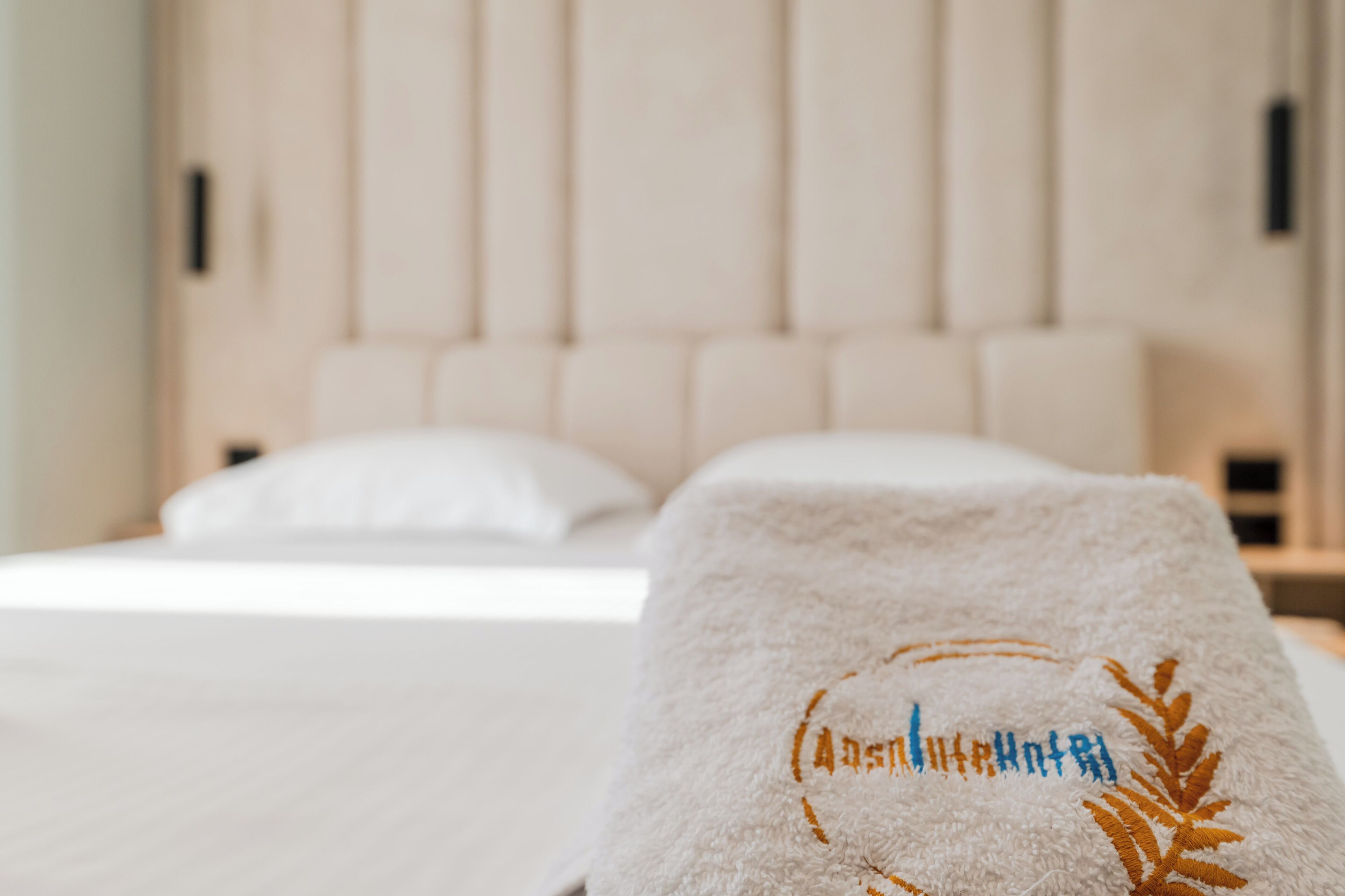 A neatly made bed with a white bedspread and a towel with embroidered text and a leaf design.