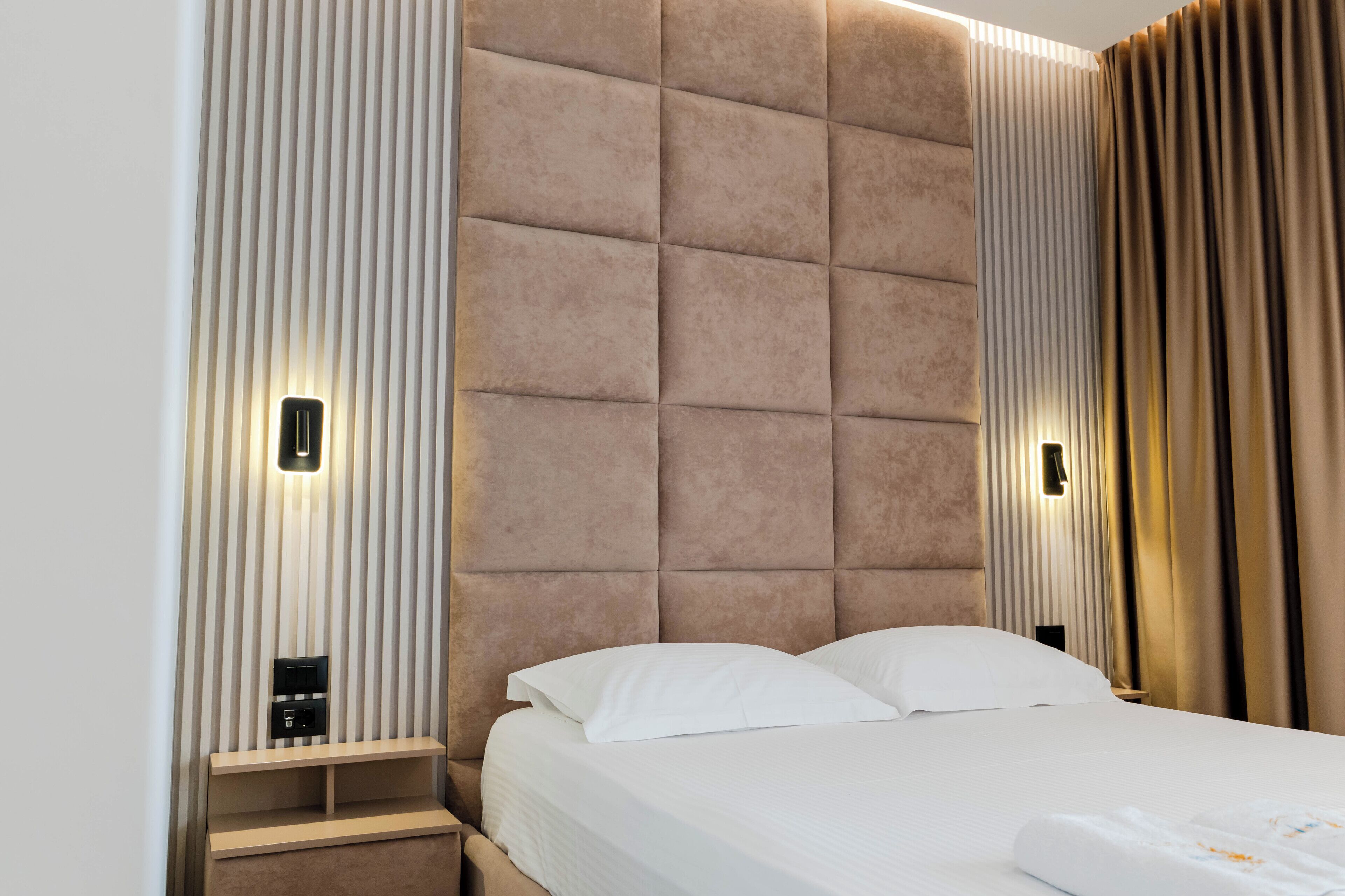 Una habitación de hotel moderna con una cama grande, cabecera acolchada e iluminación integrada.