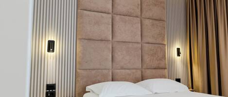 A modern hotel room with a large bed, a padded headboard, and built-in lighting.