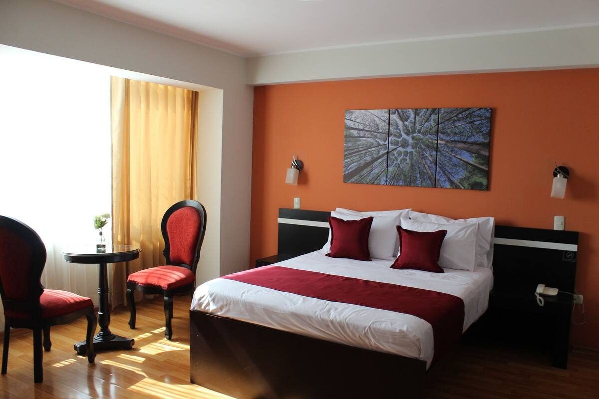 Habitación de hotel con cama, dos sillas, una mesita y un cuadro en la pared.