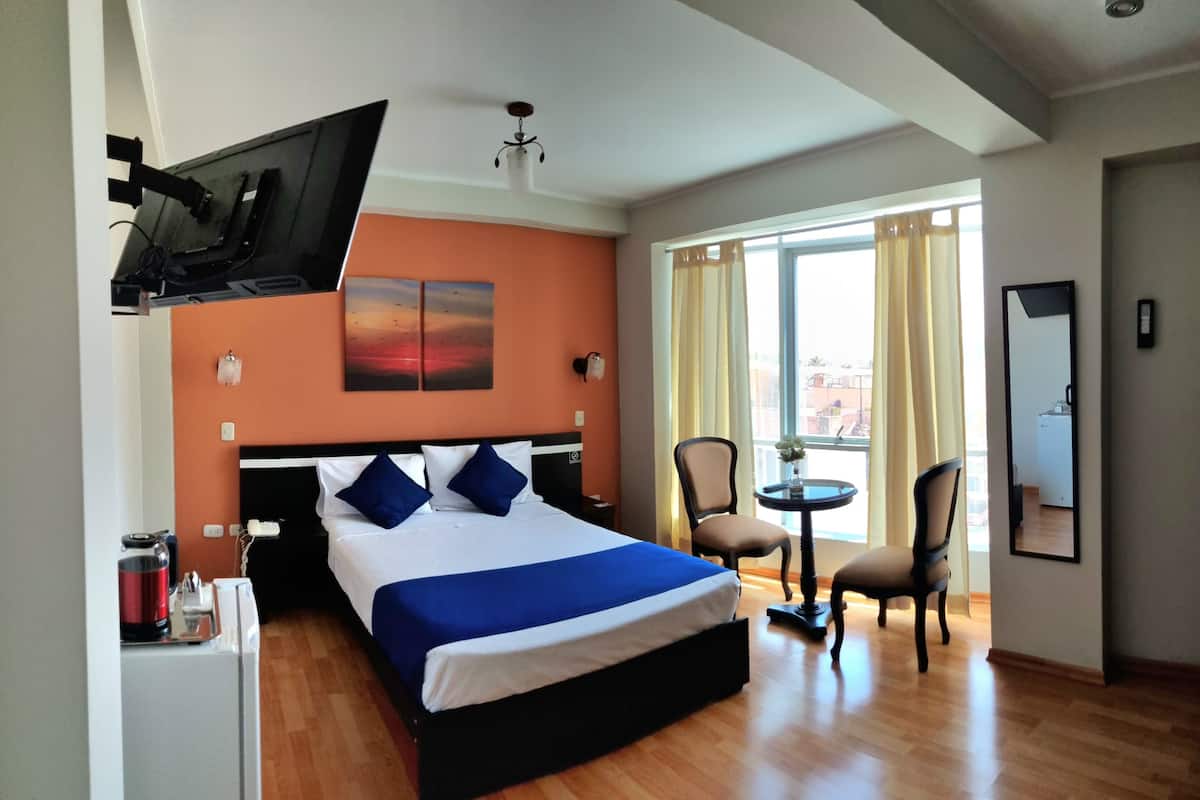 Una habitación de hotel con cama, televisión montada en la pared, escritorio con silla y ventana con cortinas.