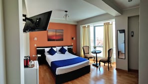 Ein Hotelzimmer mit einem Bett, einem an der Wand befestigten Fernseher, einem Schreibtisch mit Stuhl und einem Fenster mit VorhÀngen.