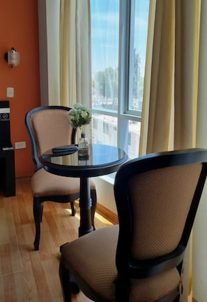 A room with a round table, two chairs, a vase with flowers, a wall socket, and a view through a window with curtains. - Platinium Hotel (Tacna)